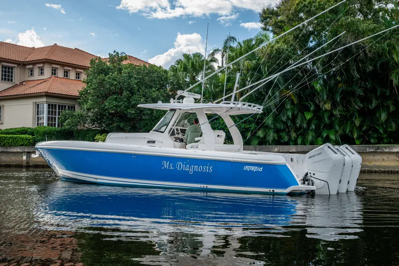 Mrs Diagnosis Yacht Photos Pics 2020 Intrepid 407 Panacea boat, blue hull, docked near waterfront home, lush greenery background.
