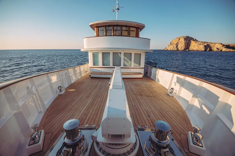 Far Niente Yacht Photos Pics Luxurious 2024 Hoek Design Motor Yacht with wooden deck, cruising near rocky coastline.