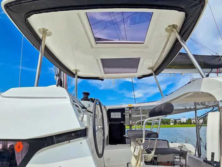 Le Tigre Yacht Photos Pics 2019 Lagoon 42 catamaran cockpit with steering wheel, skylight, and seating, under clear blue sky.