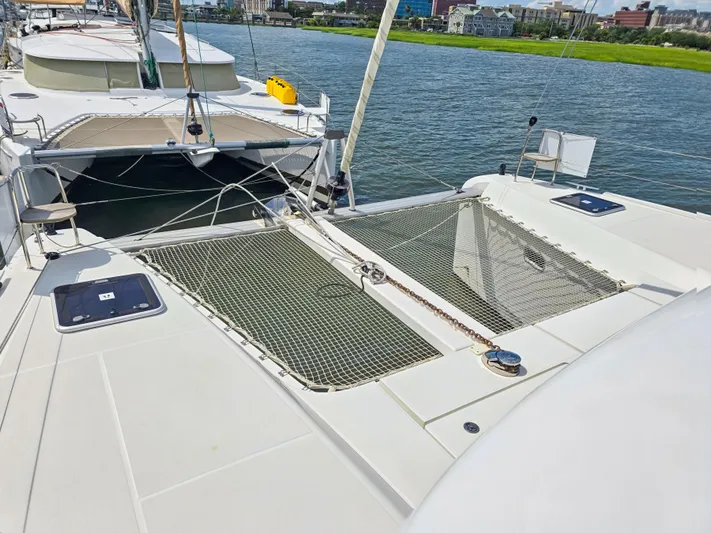 Le Tigre Yacht Photos Pics 2019 Lagoon 42 catamaran with netted deck, docked by a scenic waterfront.