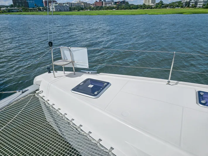 Le Tigre Yacht Photos Pics 2019 Lagoon 42 catamaran deck with netting, overlooking calm waters and distant shoreline.