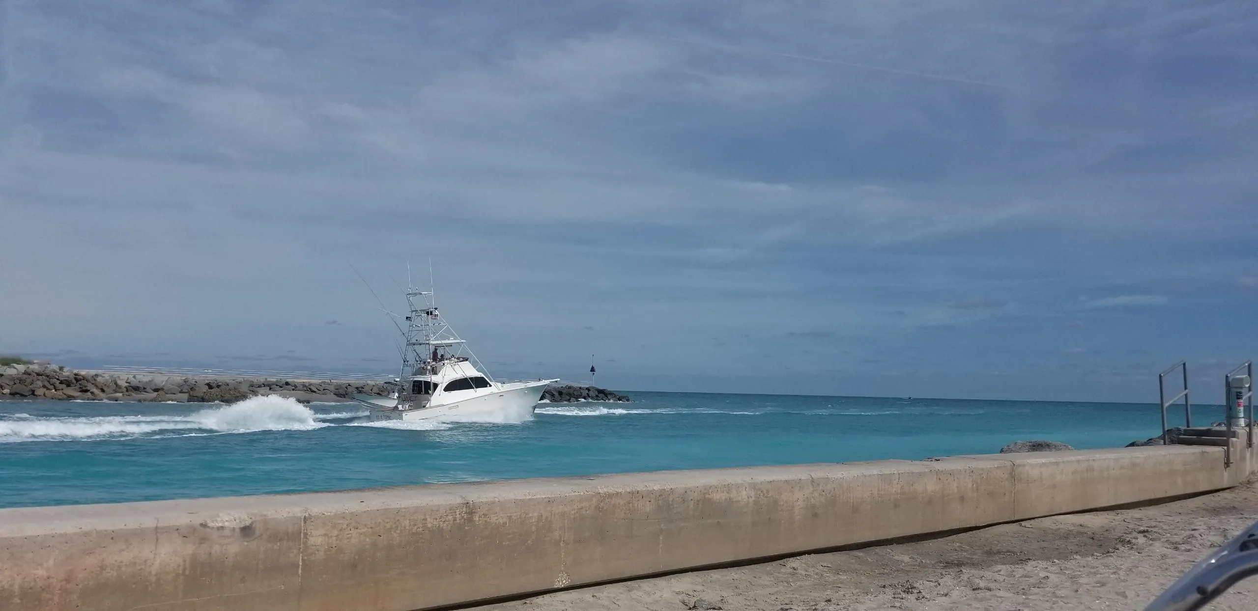 1986 Post Sportfisher boat cruising on clear blue ocean near a concrete seawall.