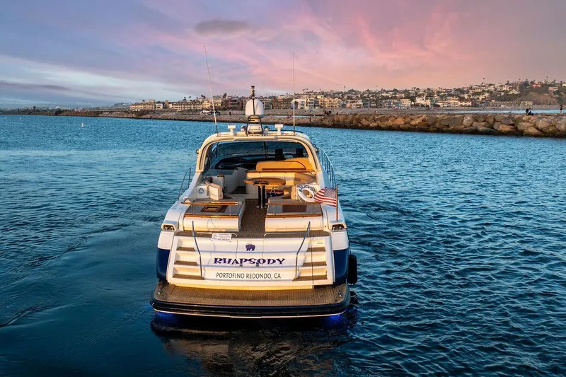 Rhapsody Yacht Photos Pics Riva 59 Mercurius yacht, 2004 model, cruising at sunset near coastal cityscape.