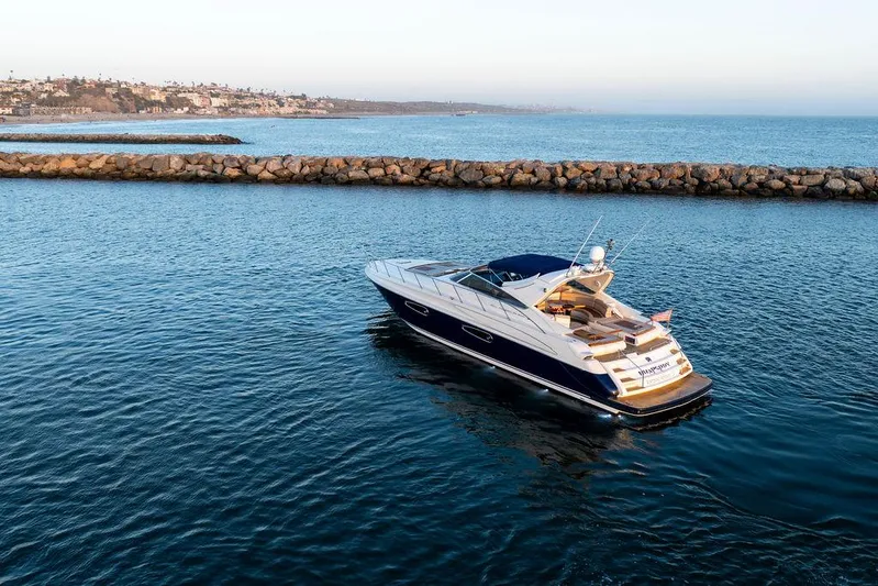 Rhapsody Yacht Photos Pics Luxury 2004 Riva 59 Mercurius yacht cruising in calm waters near rocky shoreline.