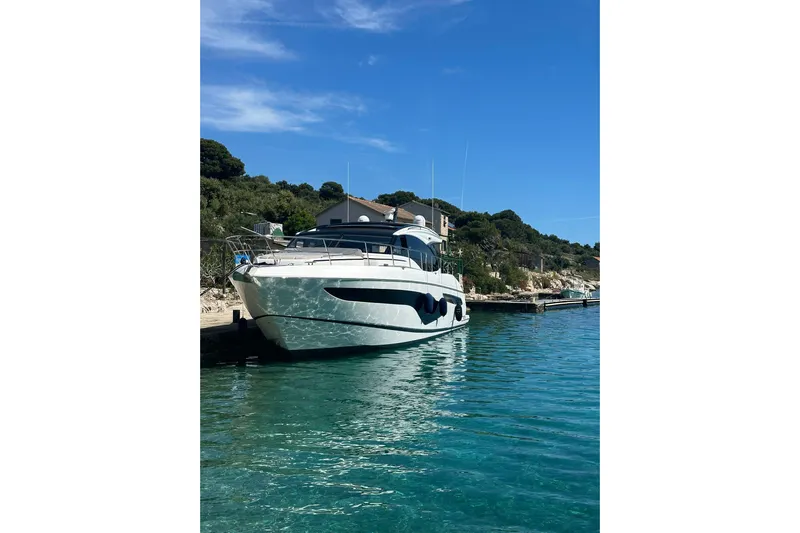 Home Office II Yacht Photos Pics 2023 Princess V60 yacht docked in clear blue water, scenic coastal backdrop.