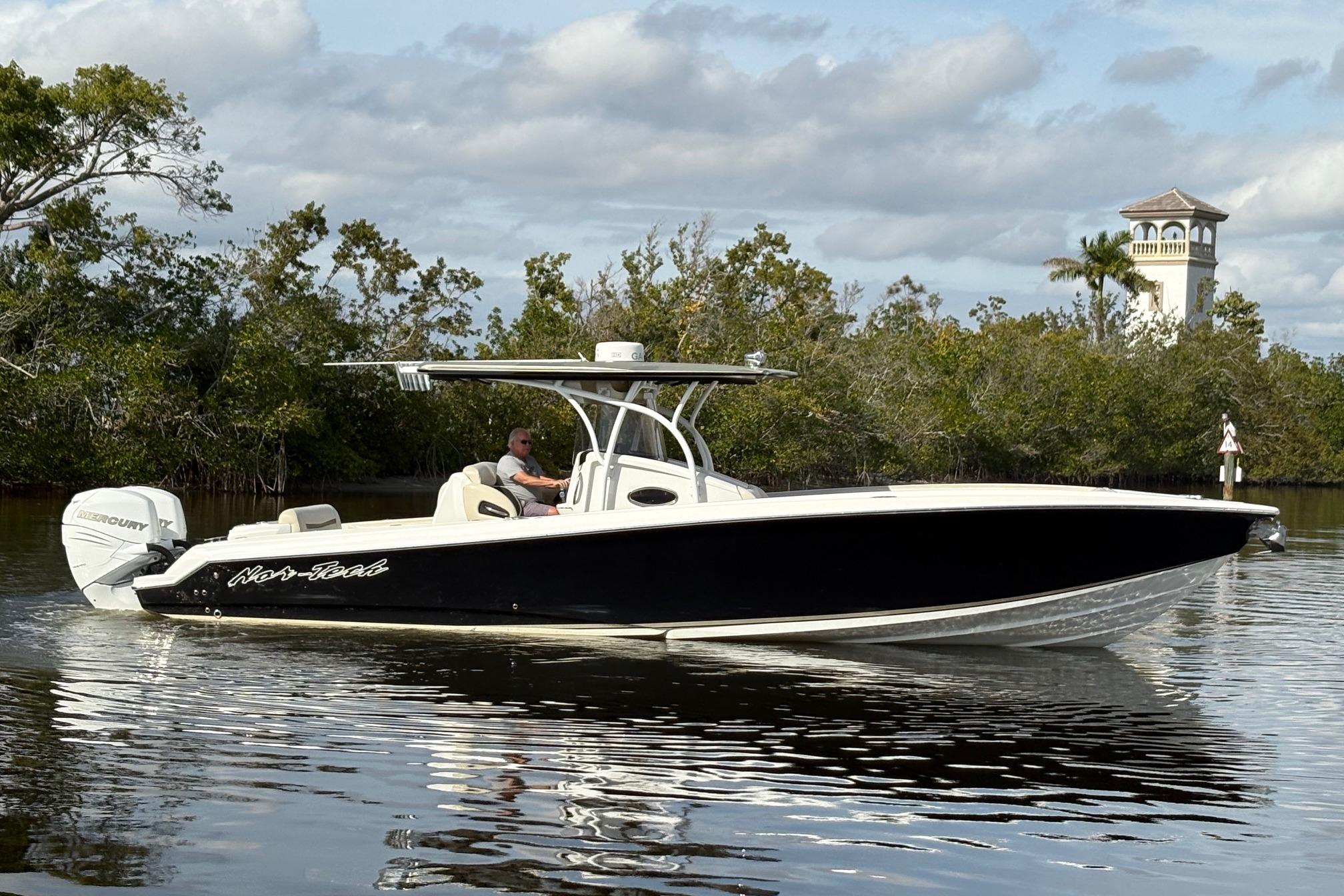 2012 Nor-Tech 340 Sport Center Console boat cruising on calm water near lush greenery.