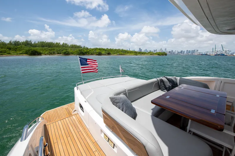 Wheelhouse Yacht Photos Pics Luxurious 2021 Princess S66 yacht with American flag, cruising near lush coastline and city skyline.