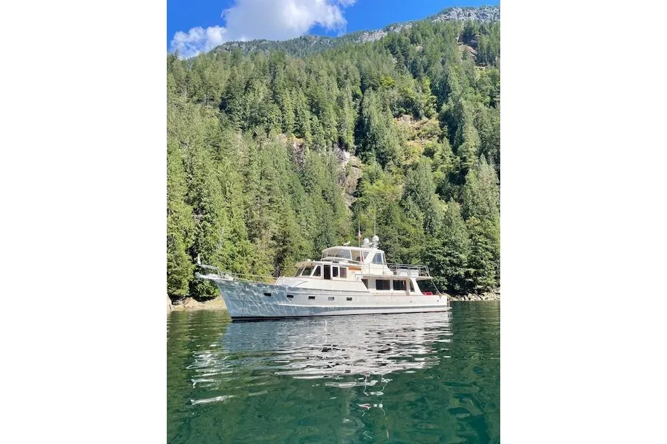 Fleming yacht from 2005 on a serene lake, surrounded by lush green forest.