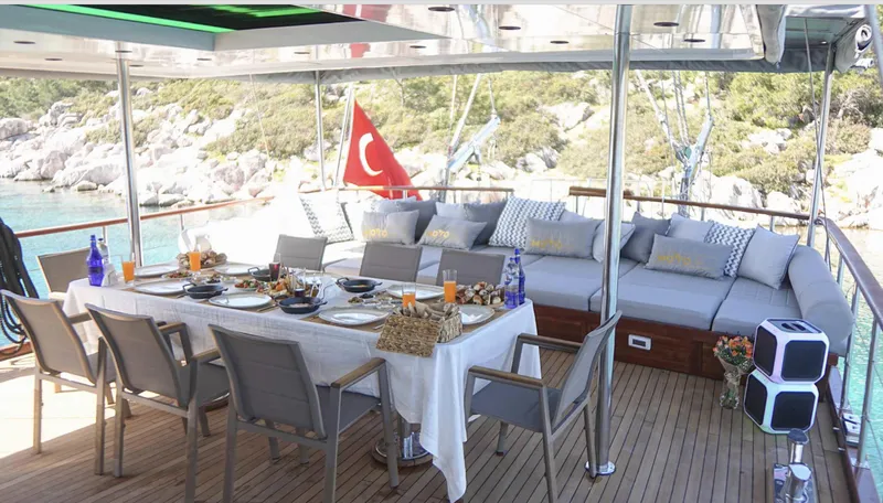  Yacht Photos Pics Luxurious 2023 Gulet yacht deck with dining area, Turkish flag, and scenic coastal view.