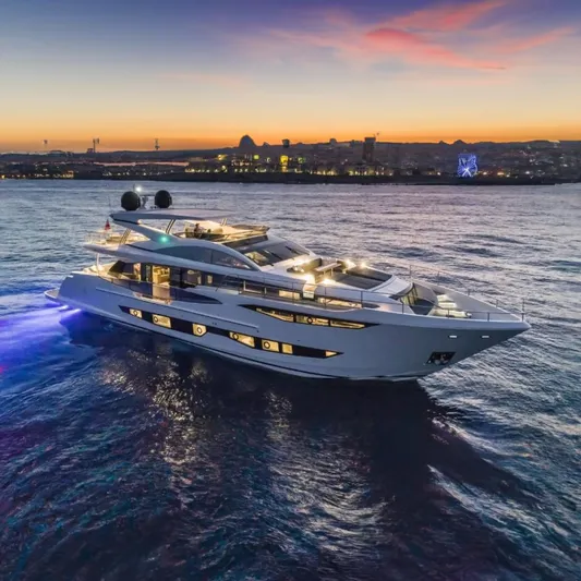  Yacht Photos Pics Luxurious 2025 Pearl 95 yacht cruising at sunset with cityscape in background.