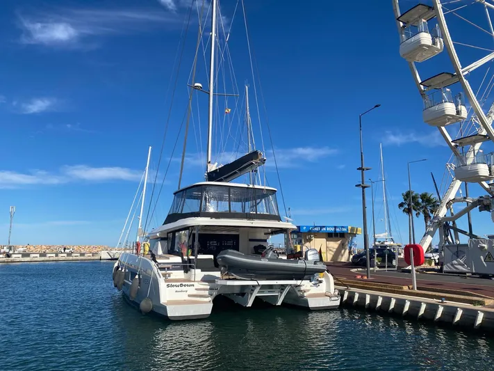 Slow Down Yacht Photos Pics 2023 Lagoon 55 catamaran docked at marina, clear blue sky, ferris wheel in background.
