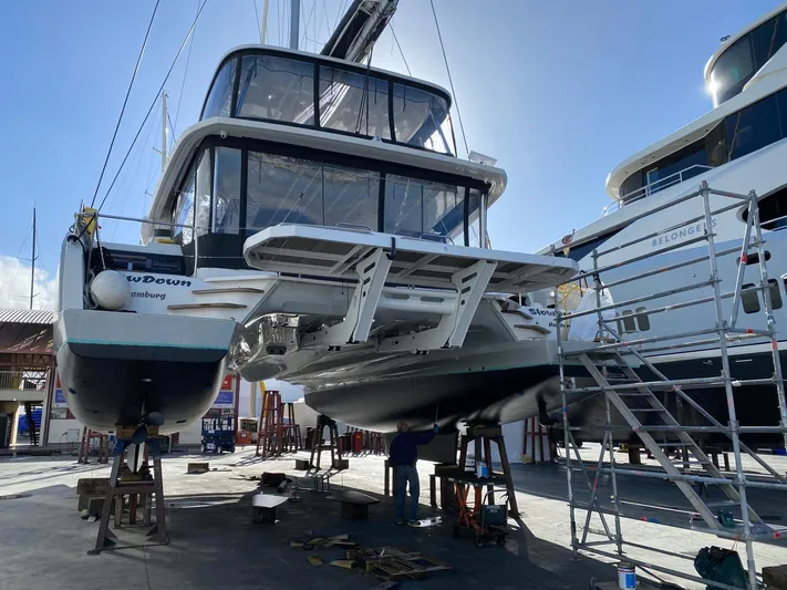Slow Down Yacht Photos Pics 2023 Lagoon 55 catamaran in a shipyard, undergoing maintenance with scaffolding.