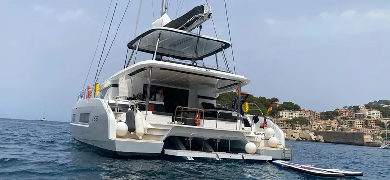 Slow Down Yacht Photos Pics 2023 Lagoon 55 yacht anchored near coastal town, with paddleboards and scenic backdrop.