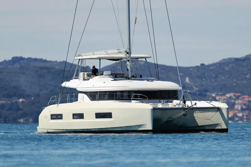 Saliska Yacht Photos Pics 2023 Lagoon 55 catamaran sailing on calm waters with scenic mountain backdrop.