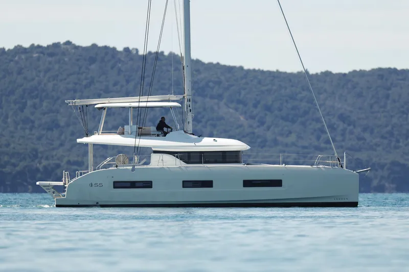 Saliska Yacht Photos Pics 2023 Lagoon 55 yacht sailing on calm waters with forested hills in the background.