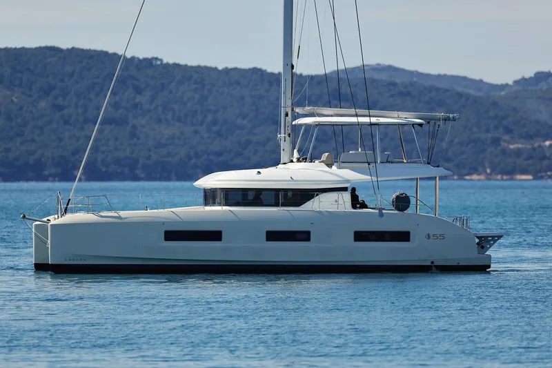 Saliska Yacht Photos Pics 2023 Lagoon 55 catamaran sailing on calm waters with scenic mountain backdrop.