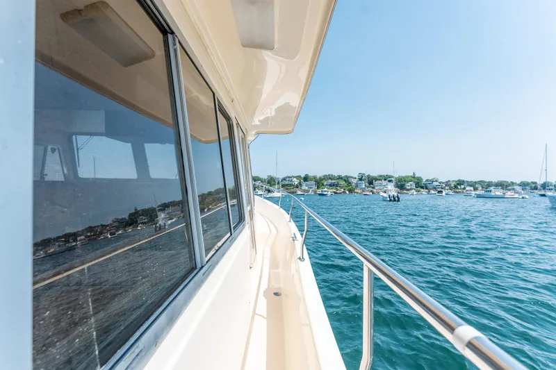  Yacht Photos Pics Side view of 2005 Mainship 400 Trawler on calm water near a coastal town.