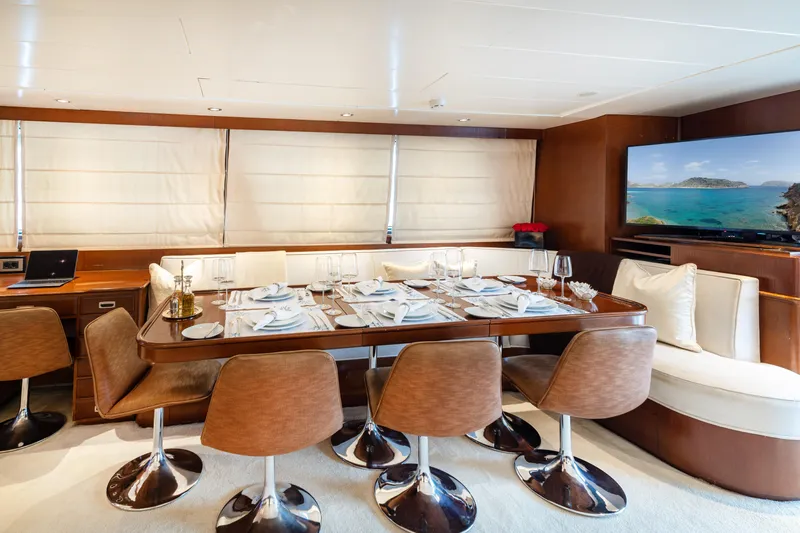Anonymous Yacht Photos Pics Luxurious yacht dining area with elegant table setting, modern chairs, and scenic ocean view on TV.