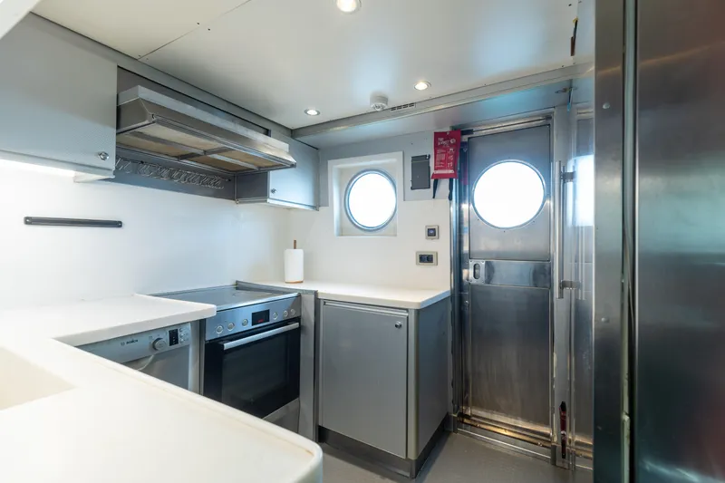 Anonymous Yacht Photos Pics Modern ship kitchen with stainless steel appliances, porthole windows, and sleek cabinetry, 1981 Hellenic Shipyards.