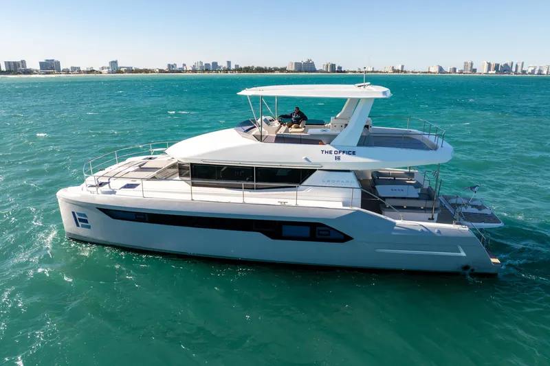 The Office Yacht Photos Pics 2021 Leopard 53 Powercat yacht cruising on turquoise waters near a city skyline.