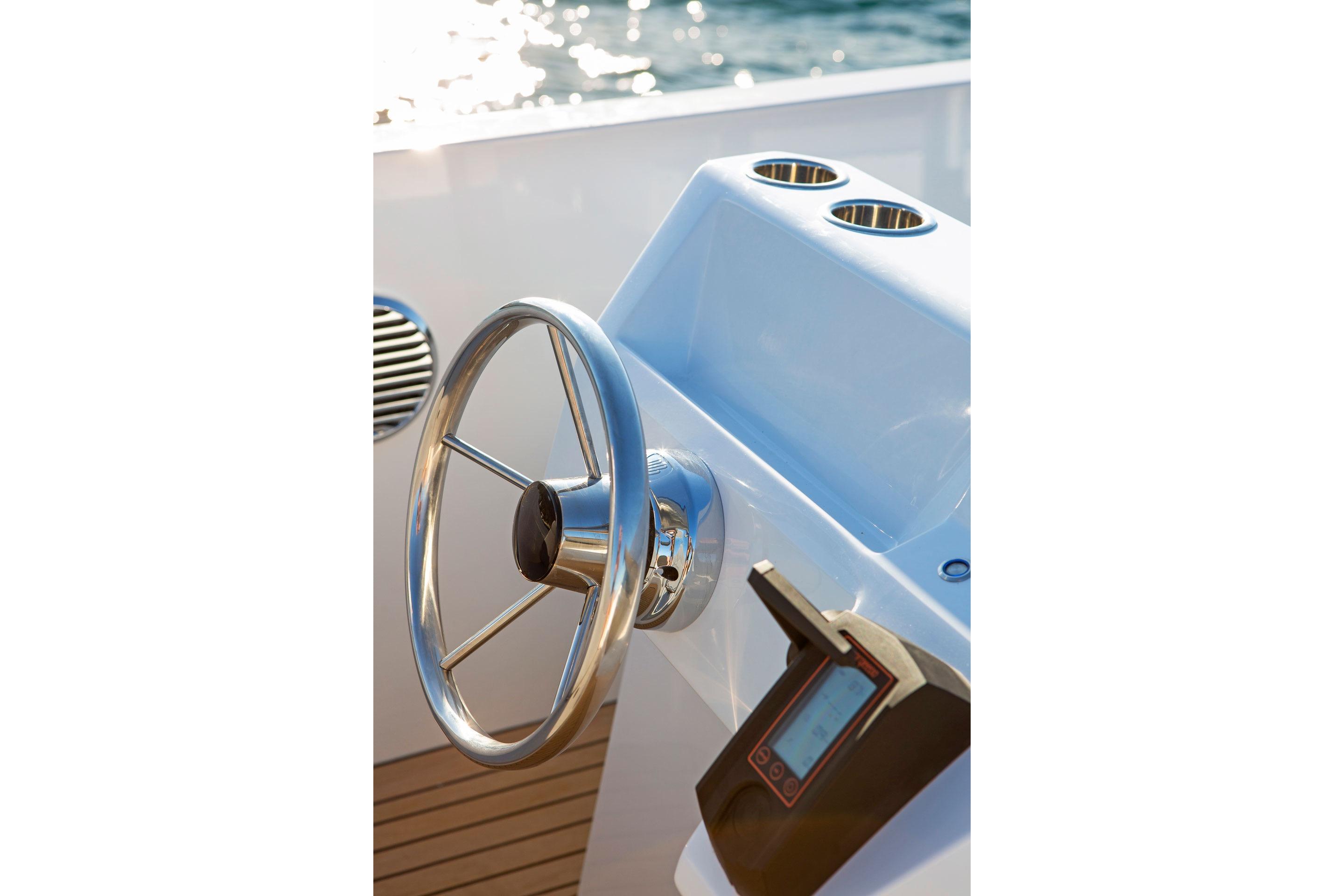 Steering wheel of 2021 Rand Mana 23 boat with control panel, sunlight reflecting on water.