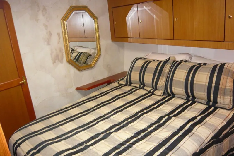 Bella Donna Yacht Photos Pics Cozy bedroom in 1999 Ocean Yachts 56, featuring striped bedding and wooden cabinetry.