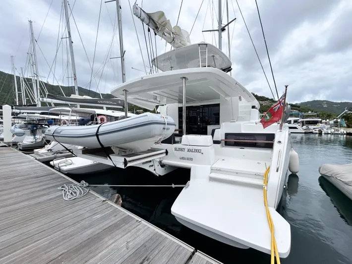 Slinky Malinki Yacht Photos Pics 2025 Lagoon 51 catamaran docked with dinghy, marina background, overcast sky.