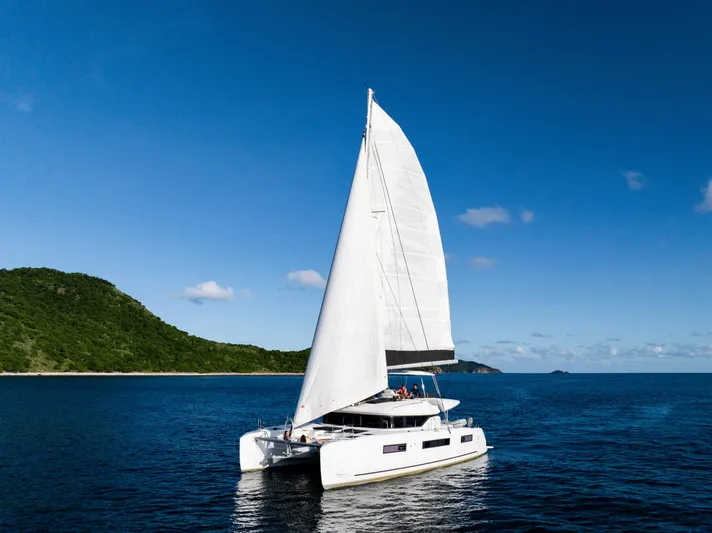 Slinky Malinki Yacht Photos Pics 2025 Lagoon 51 catamaran sailing near lush island under clear blue sky.