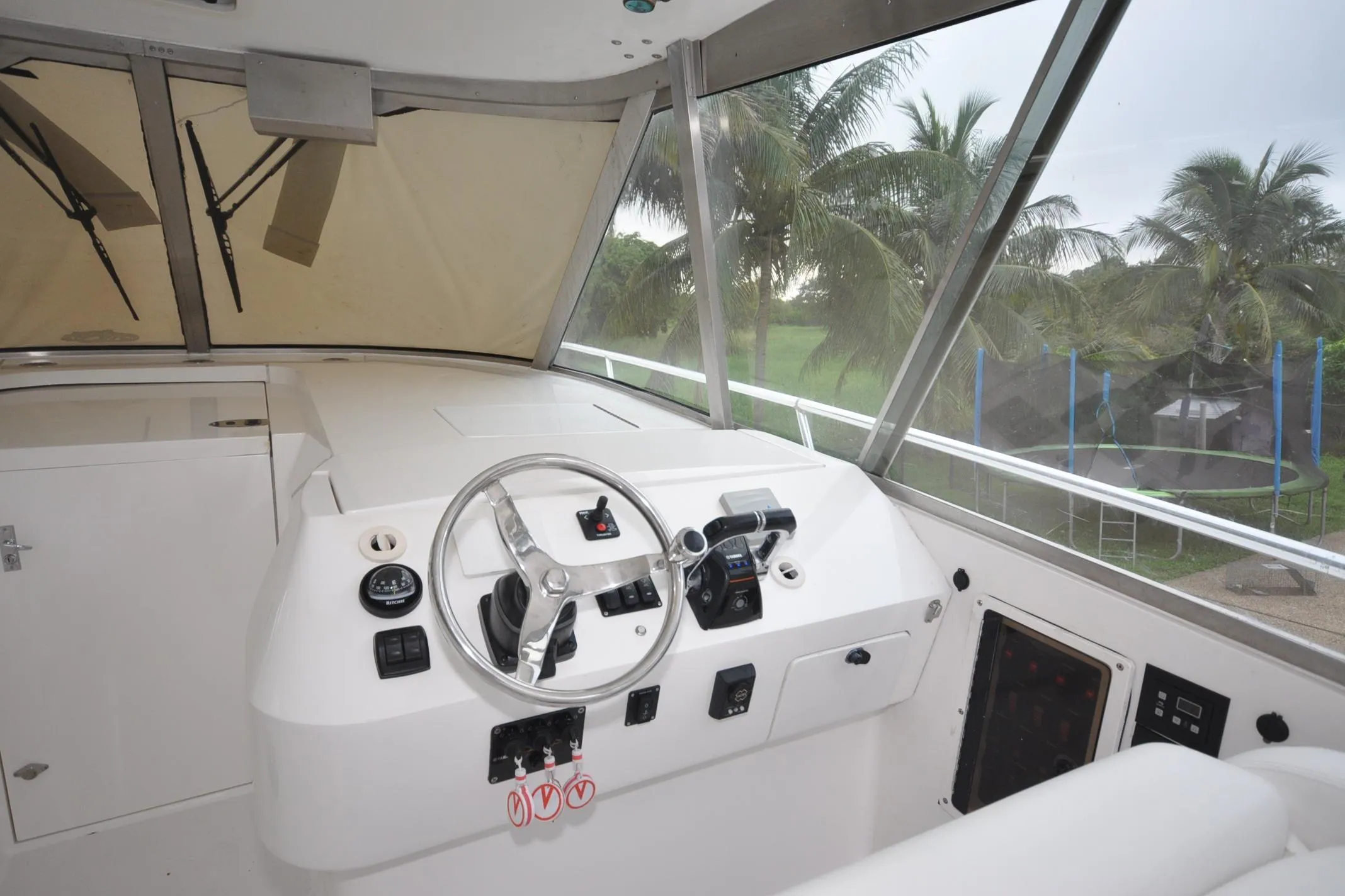 2009 Intrepid 430 Sport Yacht helm with steering wheel and controls, overlooking palm trees.