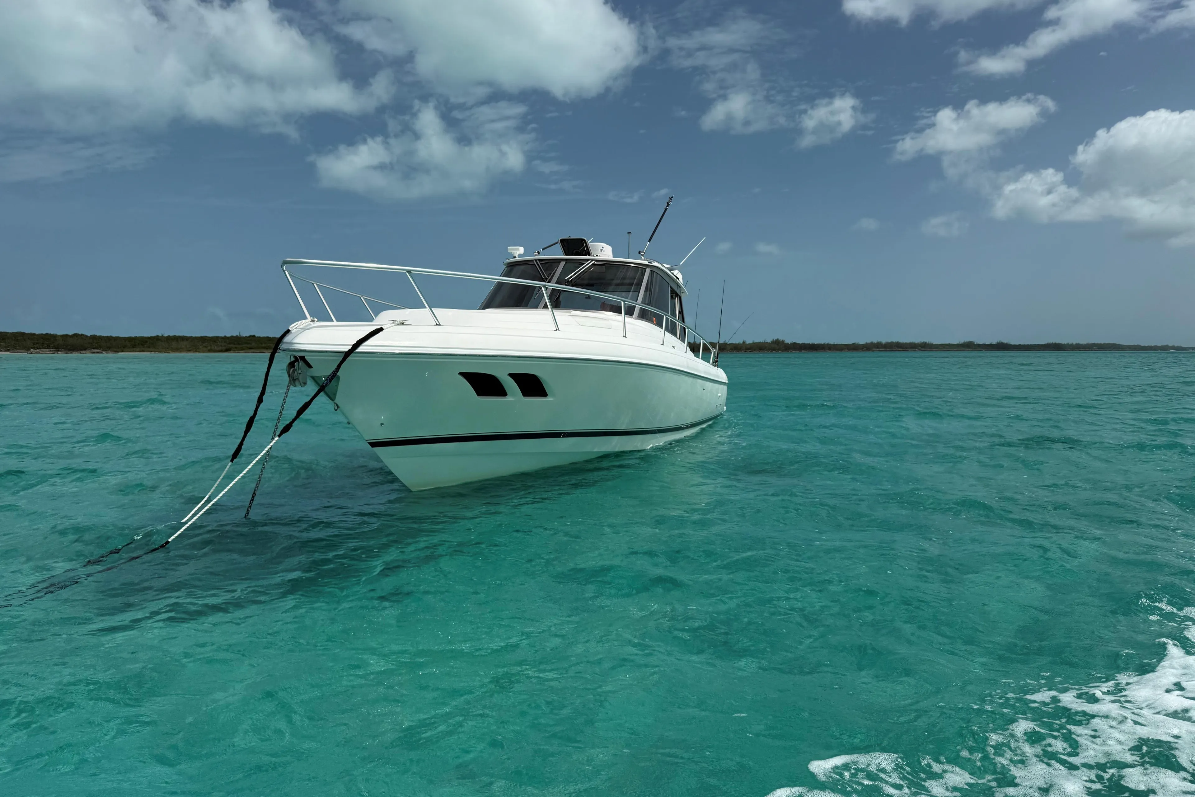 2009 Intrepid 430 Sport Yacht anchored in clear turquoise waters under a partly cloudy sky.