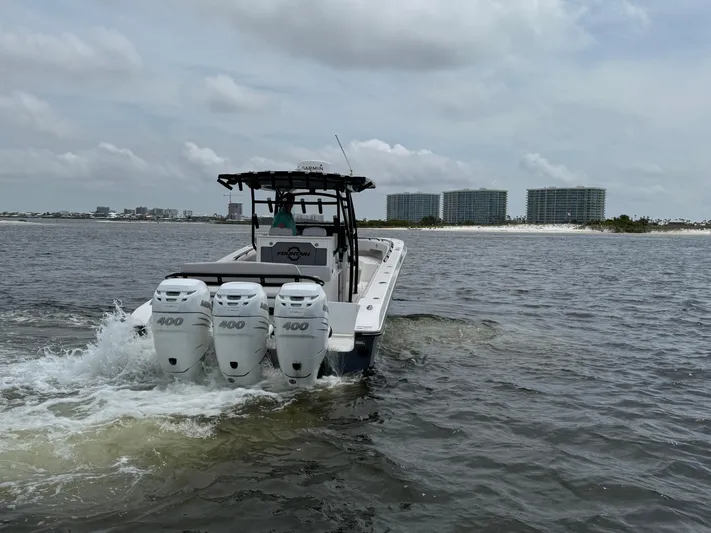  Yacht Photos Pics 2022 Fountain 38TE boat with triple engines cruising on open water near shoreline buildings.