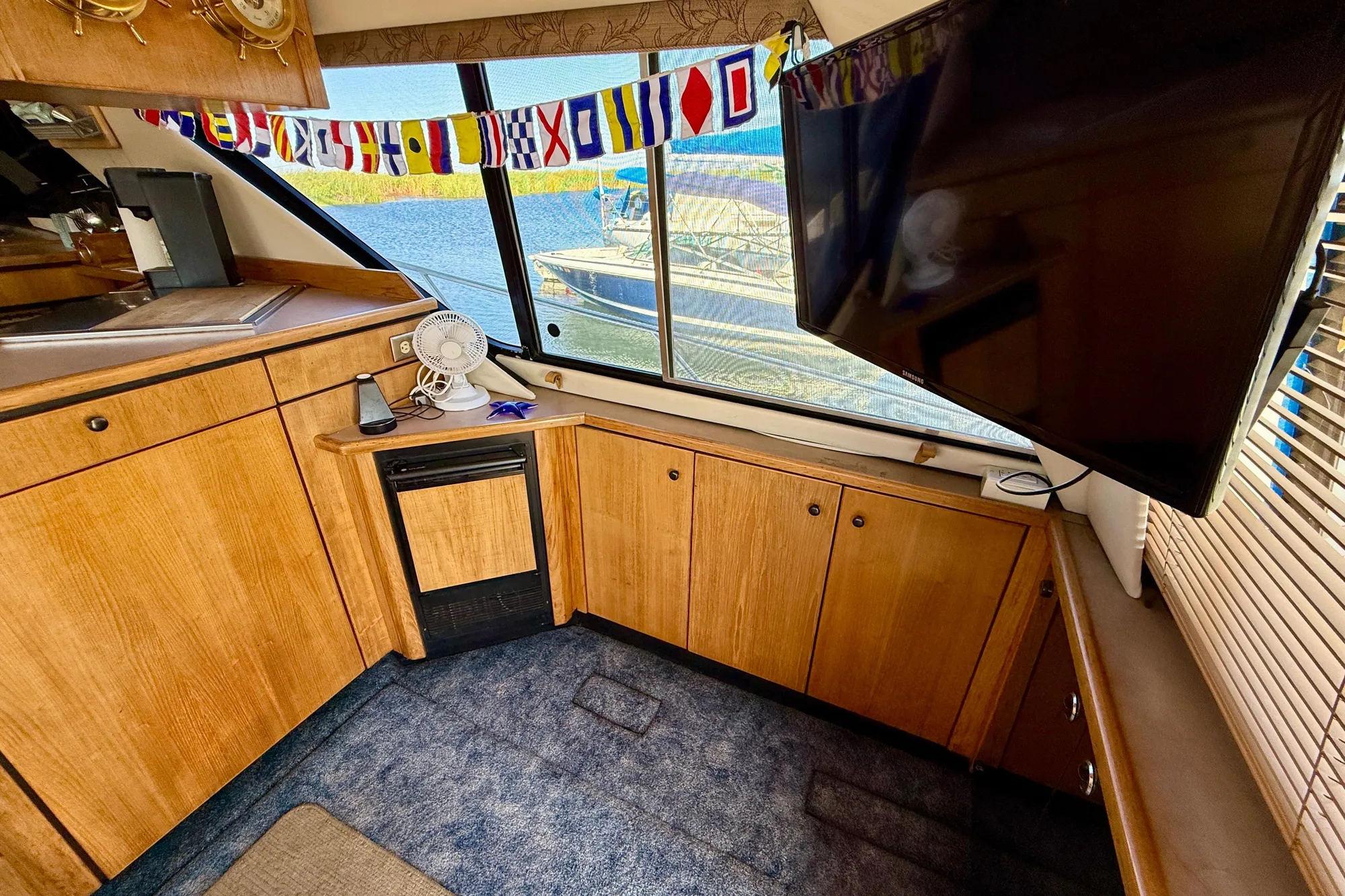 1998 Bayliner 3988 Command Bridge Motoryacht interior with wood cabinets, TV, and nautical flags.