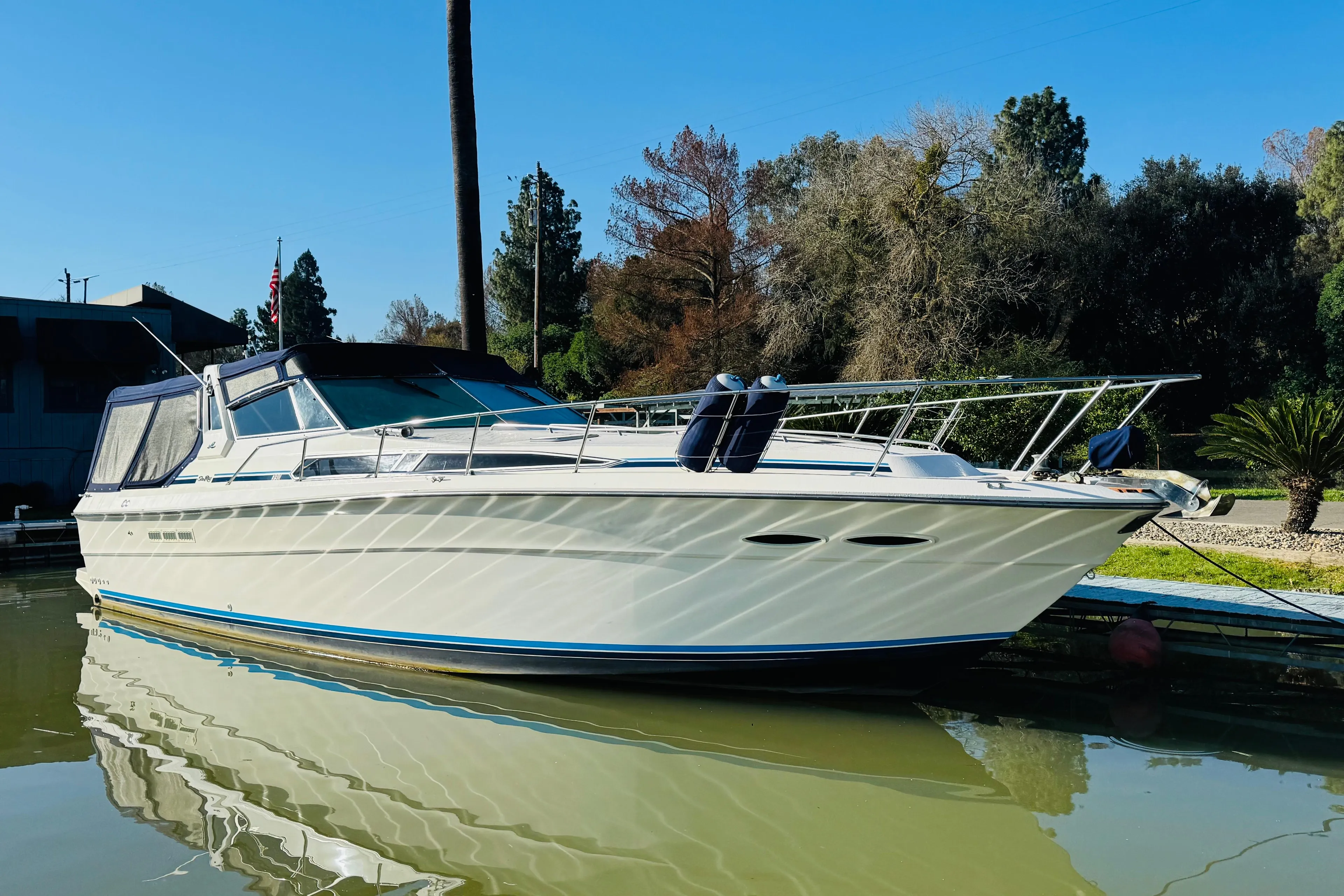 1989 Sea Ray 390 Express Cruiser docked on calm water, surrounded by trees.