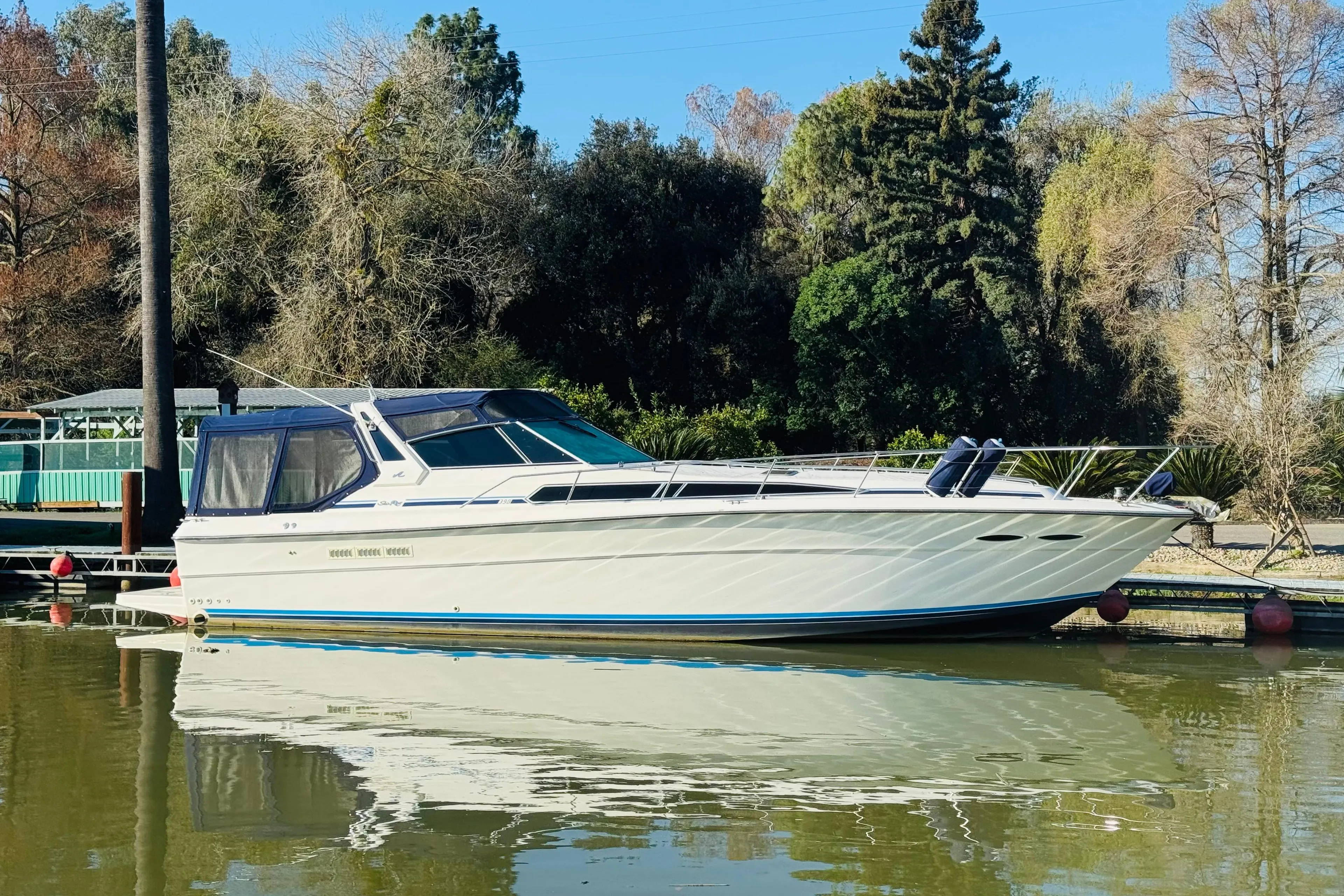 1989 Sea Ray 390 Express Cruiser docked on calm water, surrounded by trees.