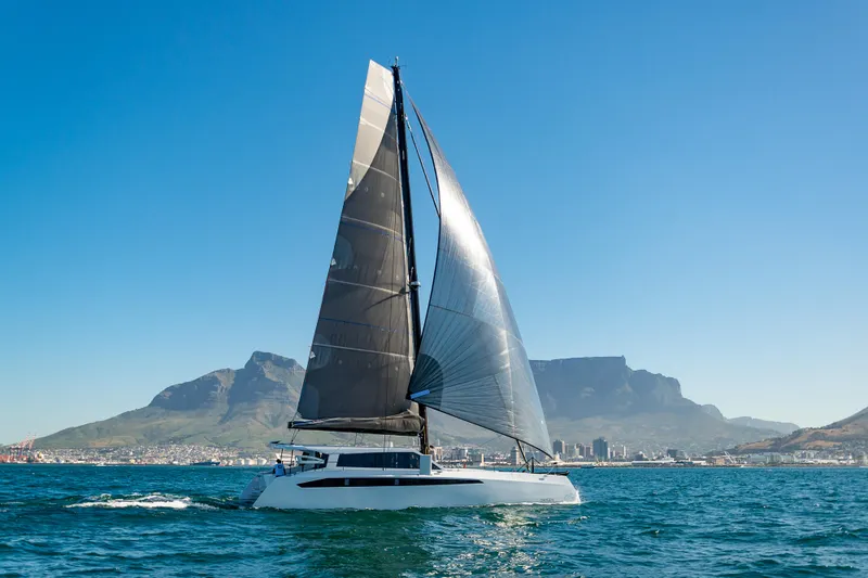  Yacht Photos Pics Ocean Renegade R6 2025 catamaran sailing on clear blue waters with mountains in the background.