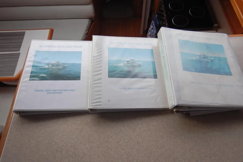Alaska Sea Duction Yacht Photos Pics Binders labeled "Alaskan Sea-Duction" with vessel documentation on a yacht's interior table.