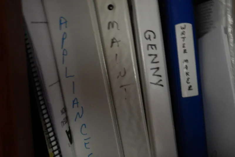 Alaska Sea Duction Yacht Photos Pics Binders labeled "Appliances," "Maint," "Genny," and "Water Maker" on a shelf, related to 1988 Camargue yacht.