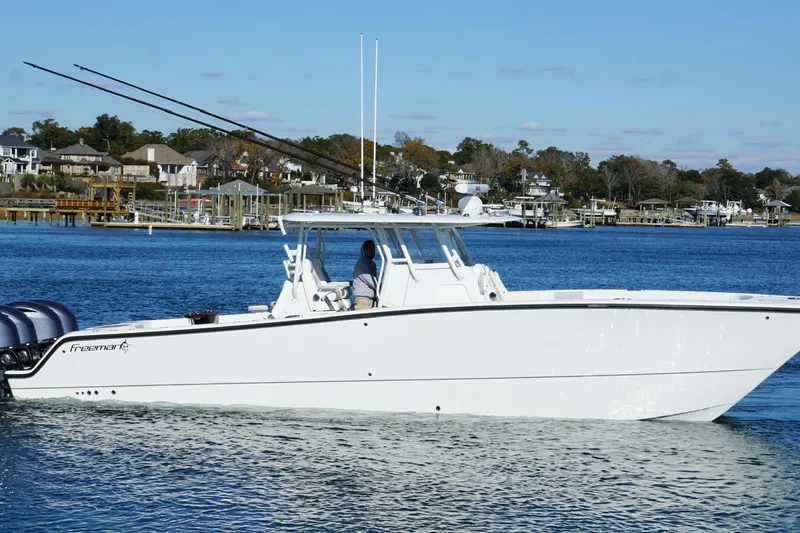  Yacht Photos Pics 2024 Freeman 38 boat cruising on a calm blue lake near a residential shoreline.