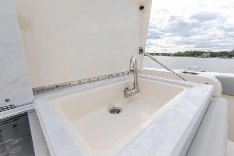 Your Next Boat! Yacht Photos Pics 2024 Scout 377 LXF boat sink with faucet, open lid, and scenic water view.