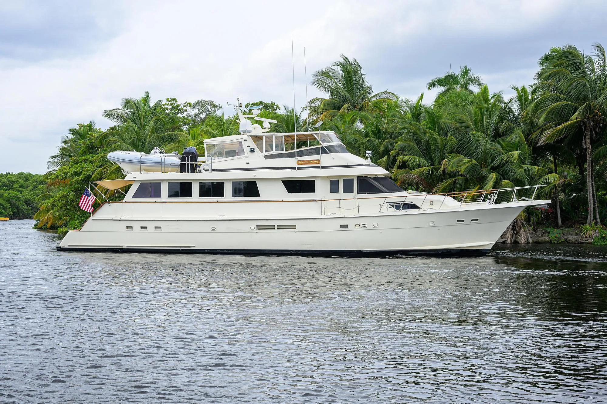 1991 Hatteras 78 CMY yacht cruising on a tropical river with lush greenery.