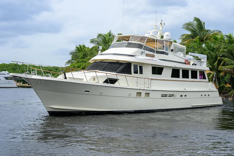 Forever Young Yacht Photos Pics Luxury 1991 Hatteras 78 CMY yacht cruising on a serene waterway, surrounded by lush greenery.