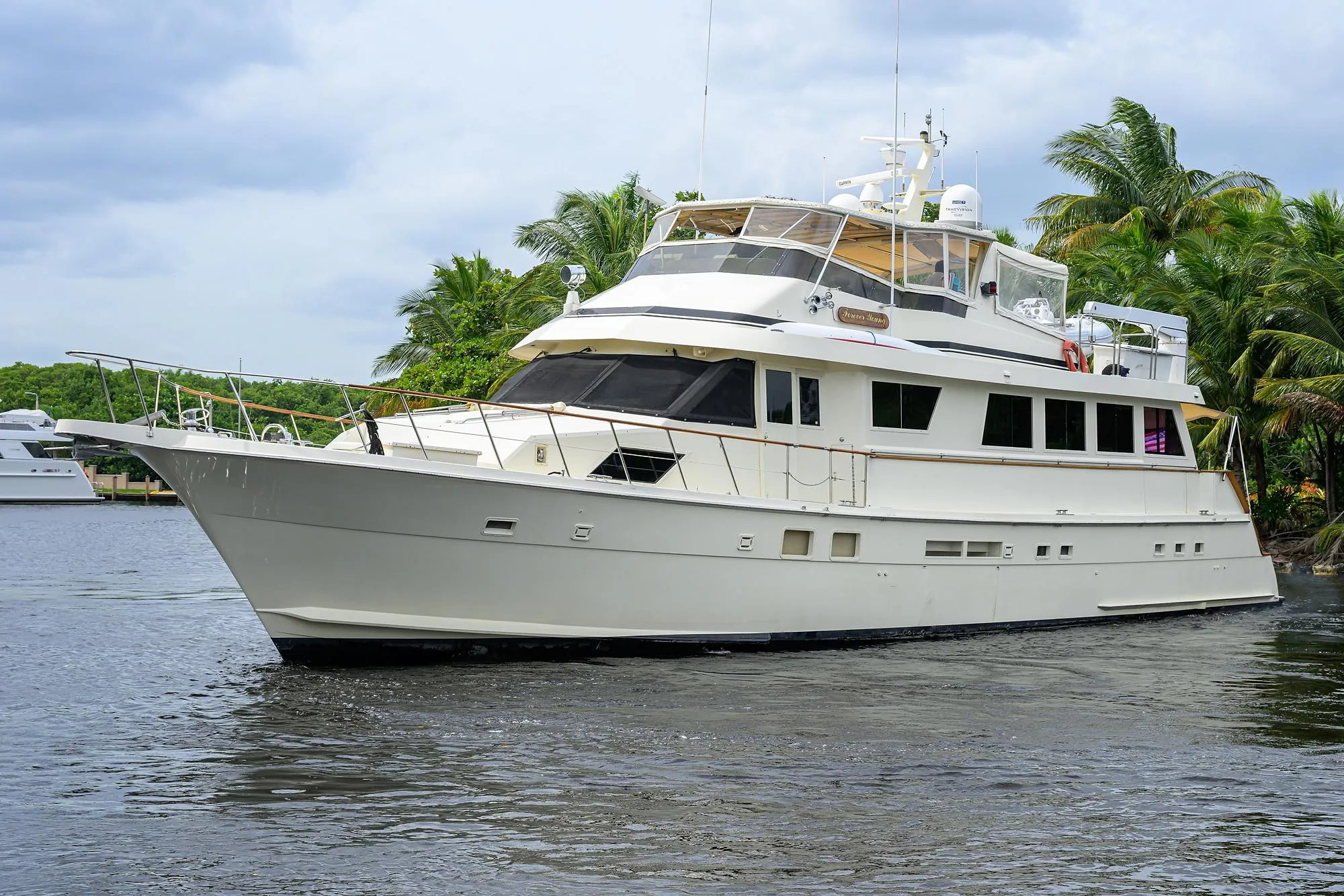 Luxury 1991 Hatteras 78 CMY yacht cruising on a serene waterway, surrounded by lush greenery.