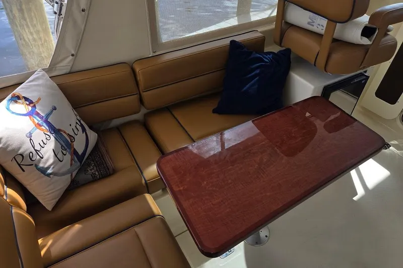 Bay'be Yacht Photos Pics Interior of 2009 Mainship Pilot 31 with brown seating, wooden table, and nautical-themed pillow.