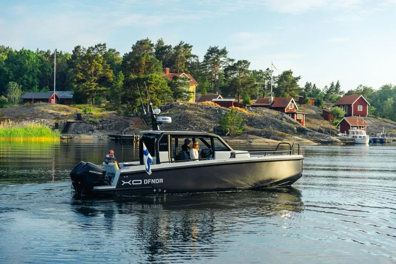Dfndr1 Yacht Photos Pics 2021 XO Boats DFNDR9 cruising near scenic shoreline with red cottages and lush greenery.