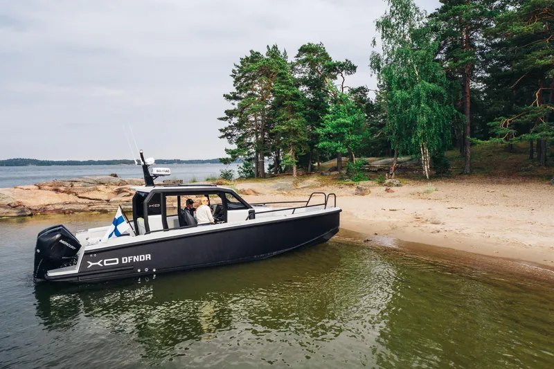 Dfndr1 Yacht Photos Pics 2021 XO Boats DFNDR9 moored on a scenic lakeside beach with lush greenery.