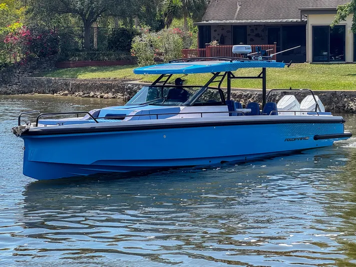  Yacht Photos Pics 2024 Axopar 37 Sun Top boat cruising on a calm waterway near a house.