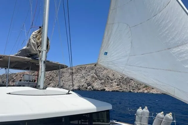 Mojito Yacht Photos Pics Lagoon 52 F catamaran sailing near rocky coastline under clear blue sky.