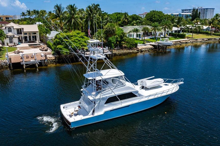 1998 Bertram 60 Convertible yacht cruising near waterfront homes and lush greenery.
