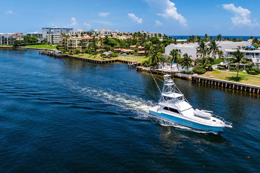 1998 Bertram 60 Convertible yacht cruising near coastal luxury homes and palm trees.