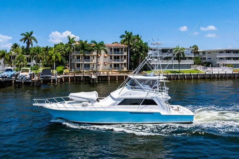 Energy Yacht Photos Pics 1998 Bertram 60 Convertible yacht cruising near waterfront homes, under clear blue skies.